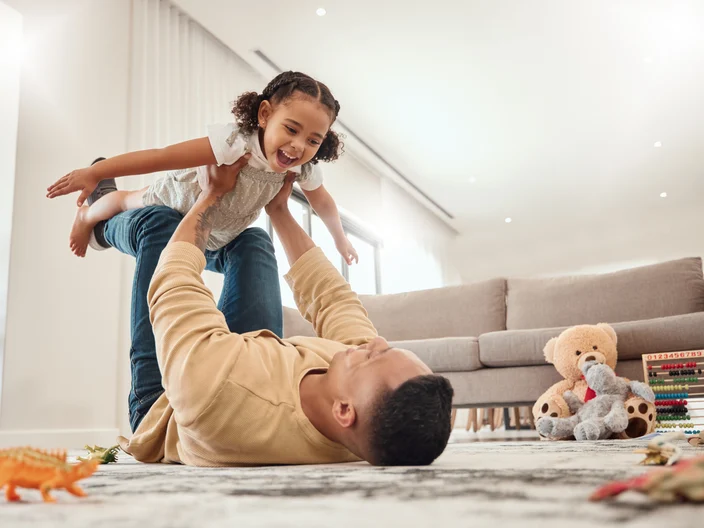 Happy family, father and girl playing in a house with freedom, bonding and enjoying quality time together. Happiness, smile and child flying in dads arms on the floor on a weekend at home in Portugal