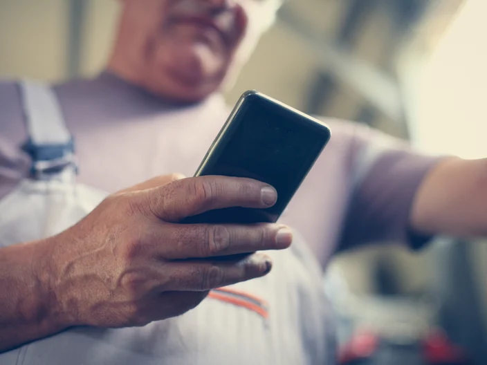Senior Man holding mobile reading text at workshop