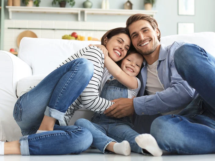 Young Caucasian family with small daughter pose relax on floor in living room, smiling little girl kid hug embrace parents, show love and gratitude, rest at home together.