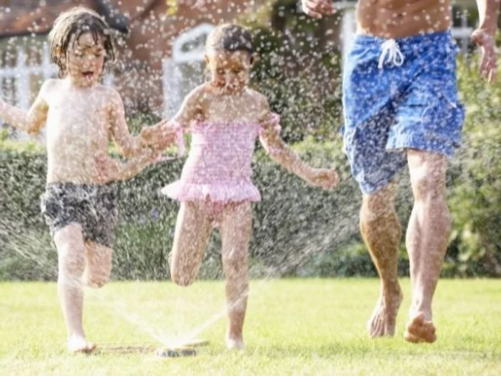 Family Staying Cool In Sprinkler