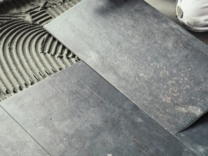 Worker placing ceramic floor tiles on adhesive surface