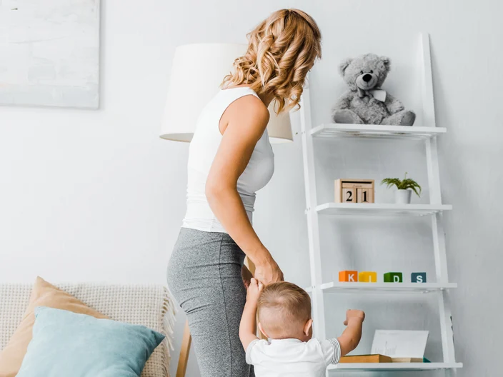mother and toddler son standing near couch and looking at rack