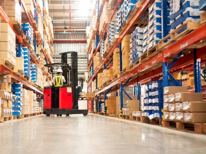 Worker in forklift truck loading packed goods in warehouse