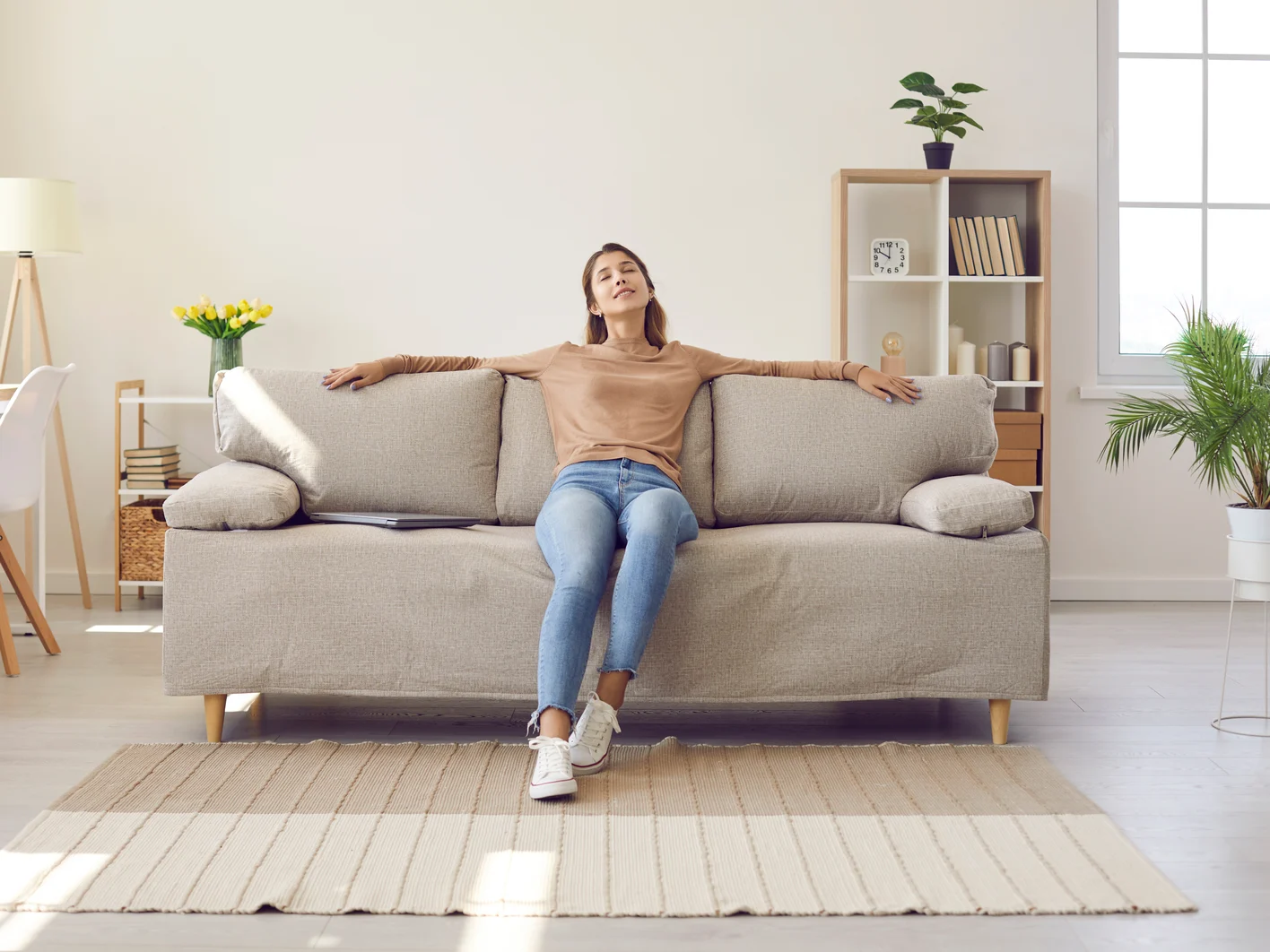 Happy relaxed young woman resting sitting on comfortable sofa in living room at home.