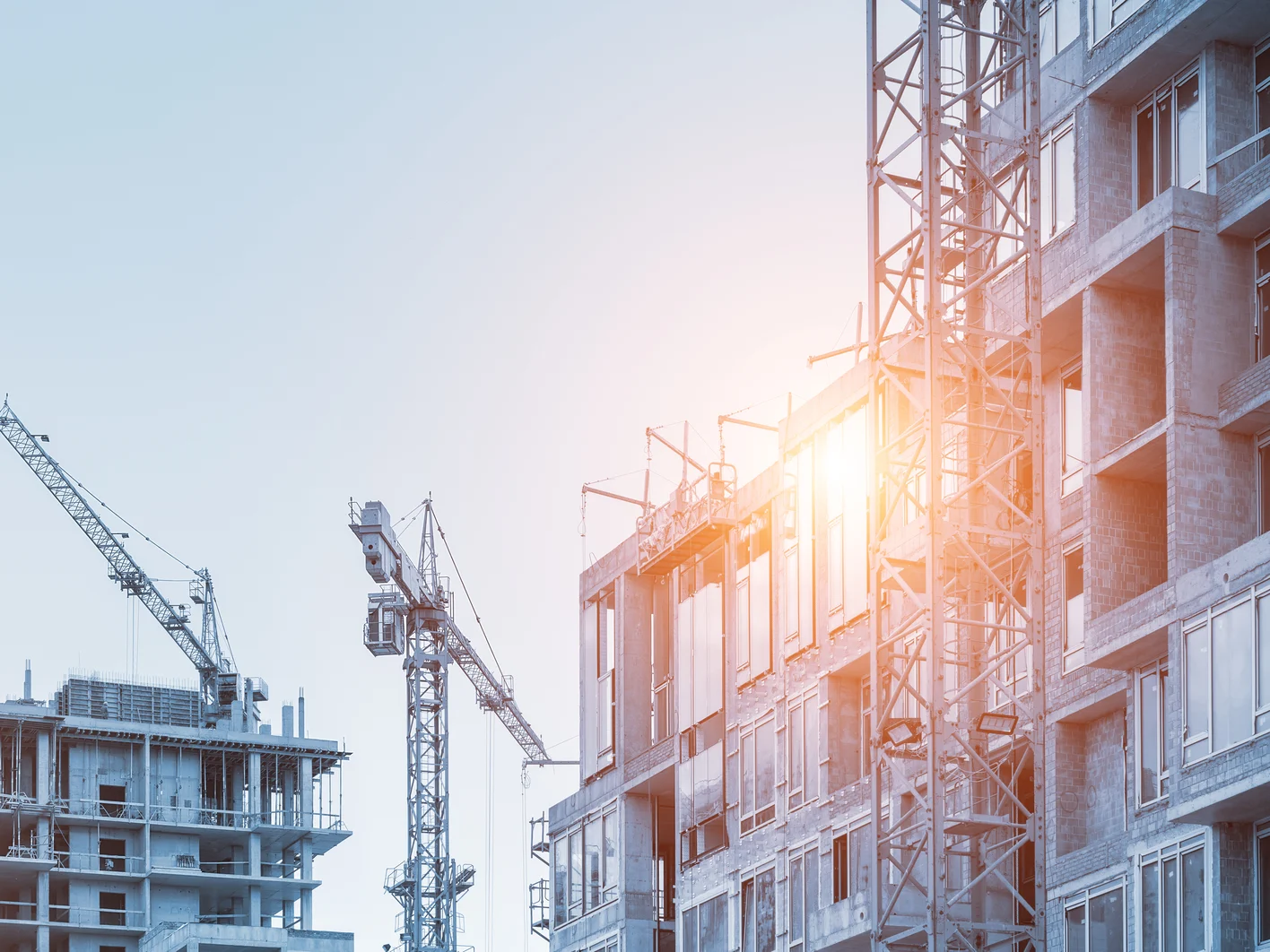 Modern apartment residential building glass facade wall construction site with many high tower cranes and heavy machinery against blue sky background. Industrial scenic urban city development project