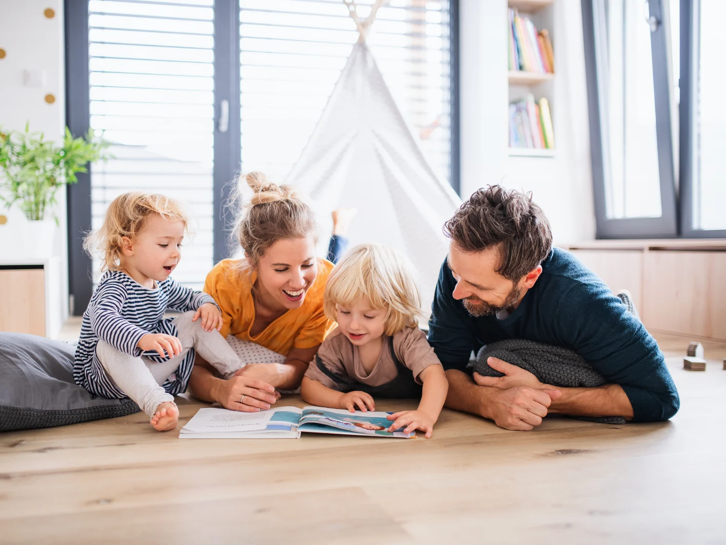 Young family with two small children indoors in bedroom reading 