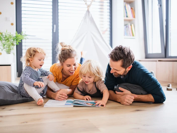 Young family with two small children indoors in bedroom reading 