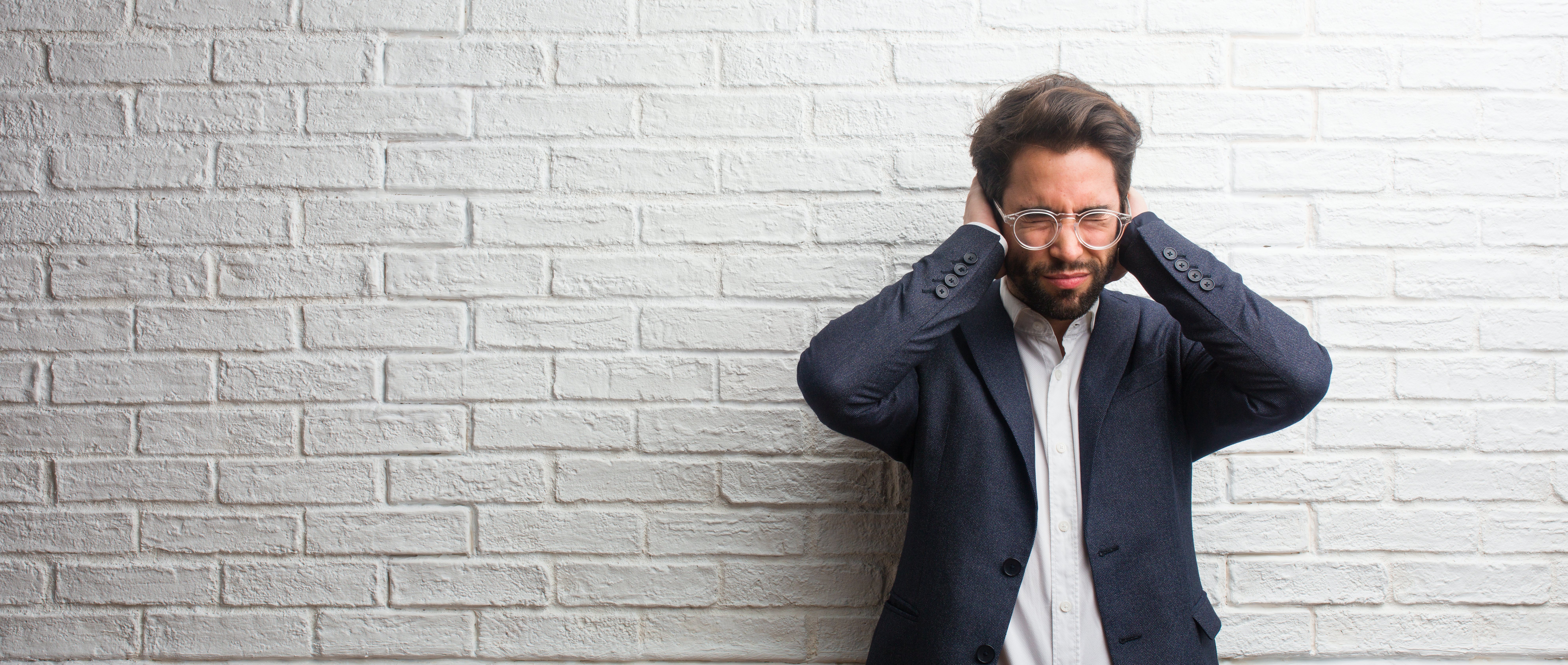 Young friendly business man covering ears with hands, angry and tired of hearing some sound