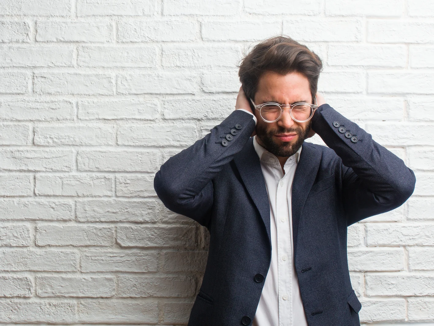 Young friendly business man covering ears with hands, angry and tired of hearing some sound