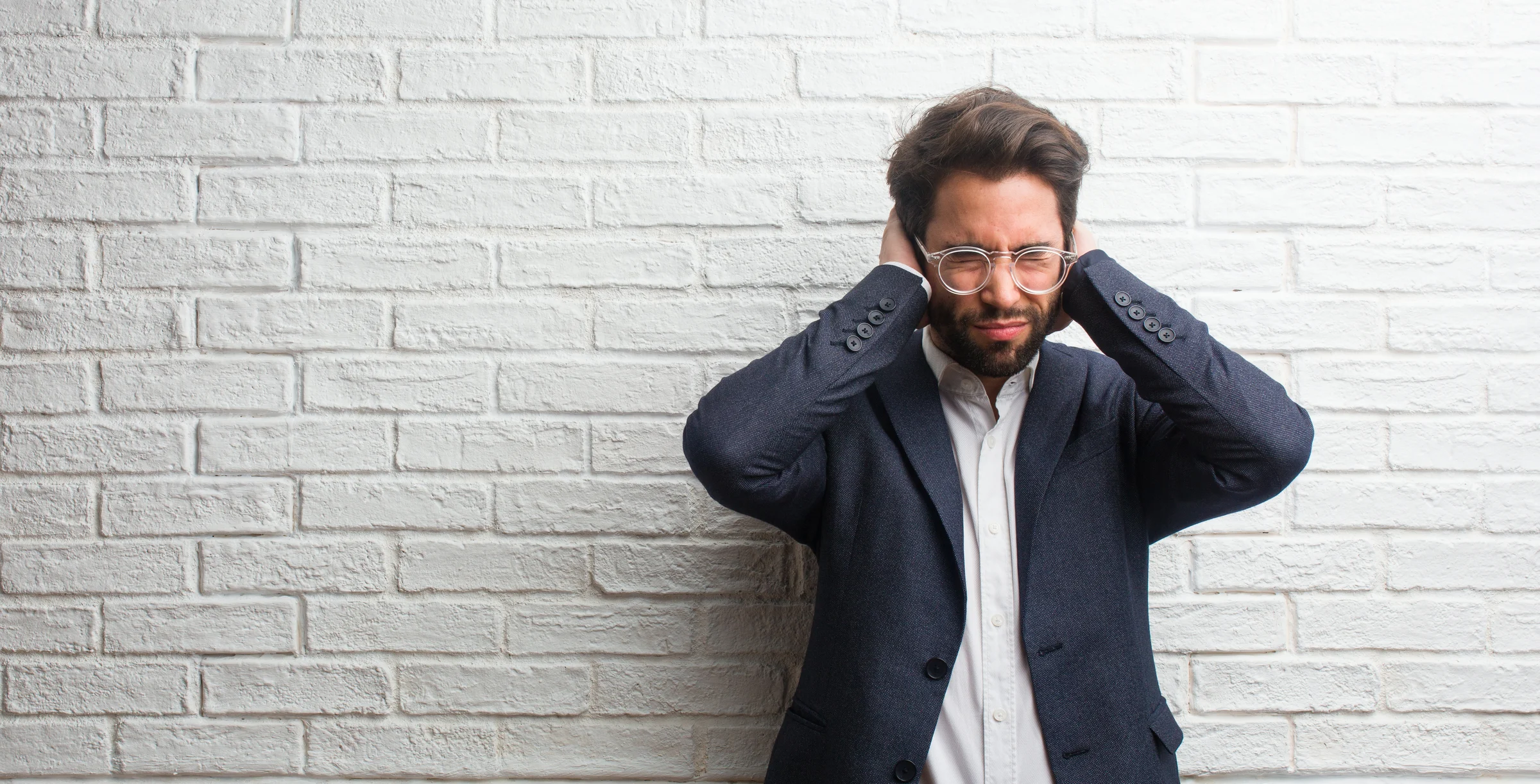 Young friendly business man covering ears with hands, angry and tired of hearing some sound