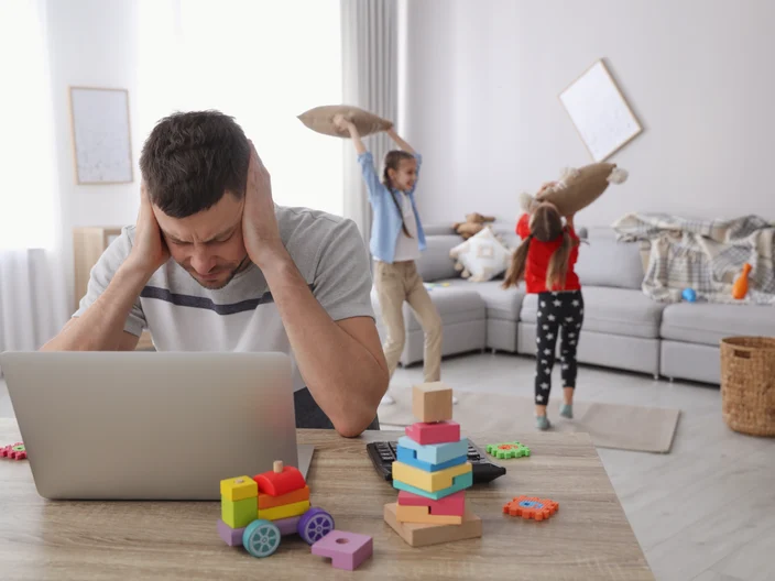 Children disturbing stressed man in living room. Working from home during quarantine
