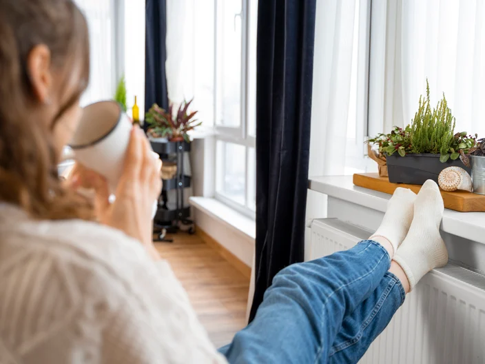 Woman sitting with feet on radiator drinking