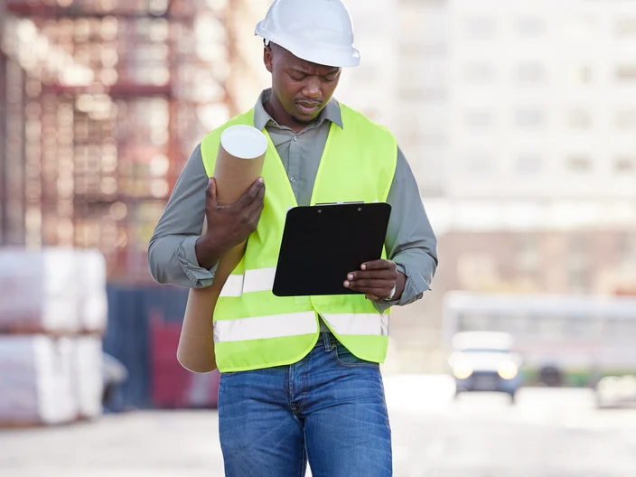 onstruction worker standing with blueprints and clipboard on a building site