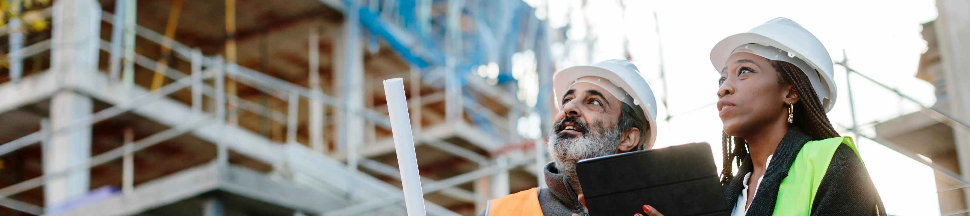 Woman engineer supervising construction of building with construction worker checking her tablet device