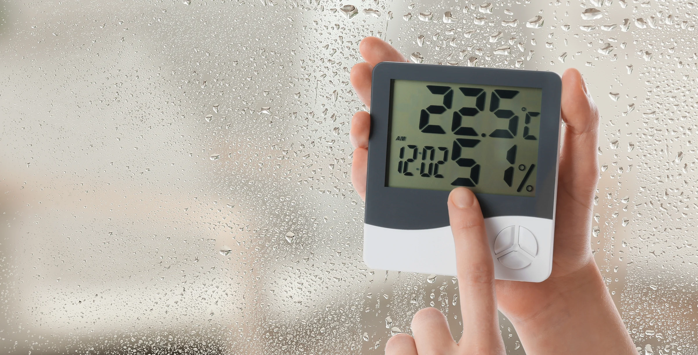 Woman holding digital hygrometer with thermometer near window on rainy day, closeup. Space for text