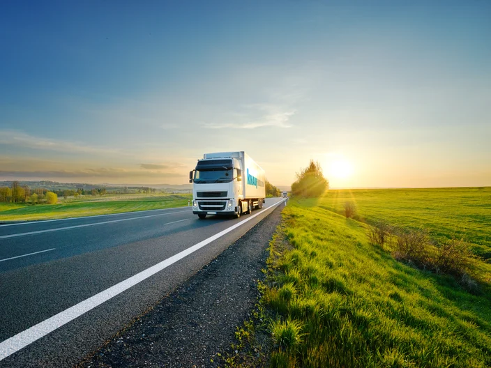 White truck driving on the asphalt road in rural landscape at sunset