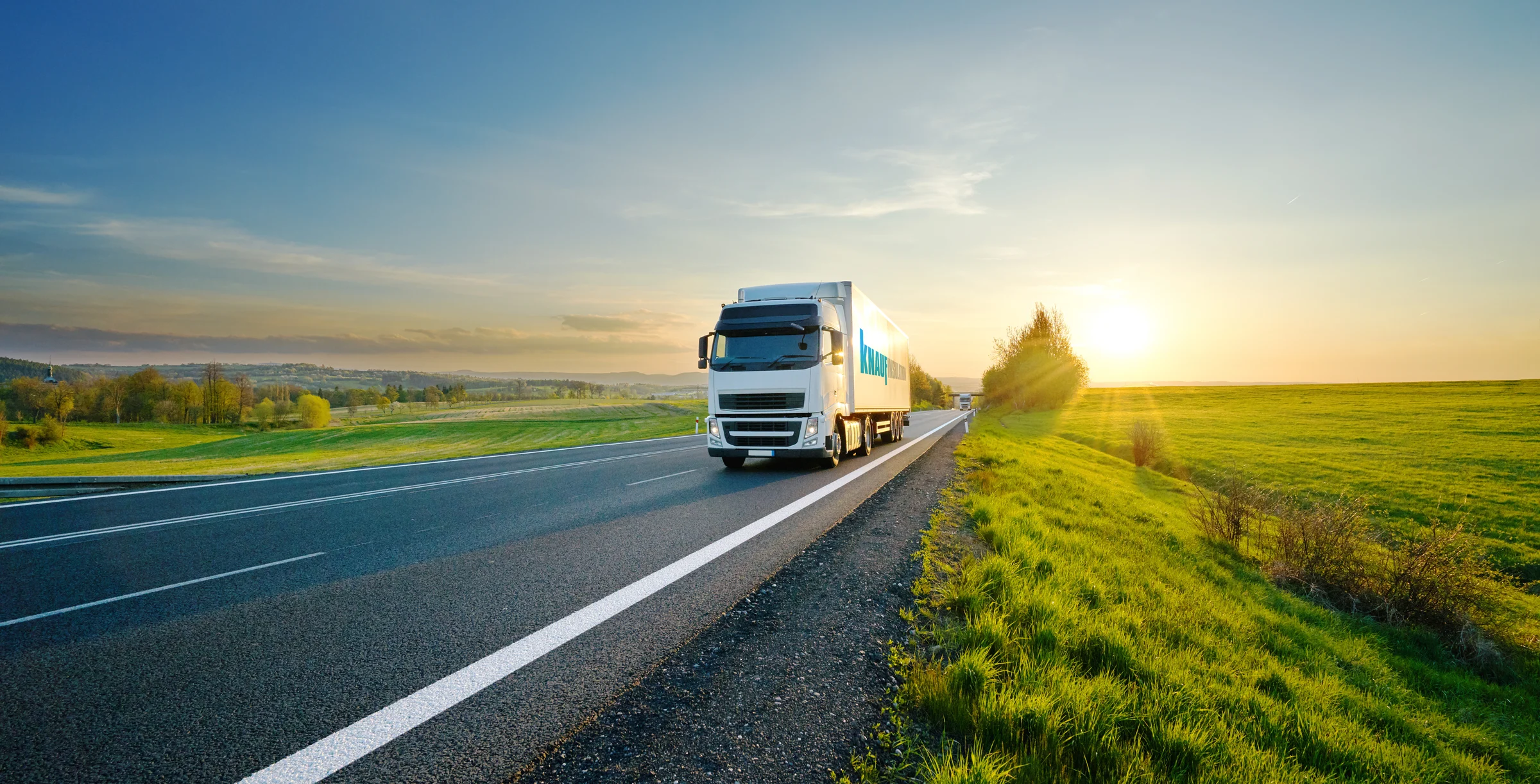 White truck driving on the asphalt road in rural landscape at sunset