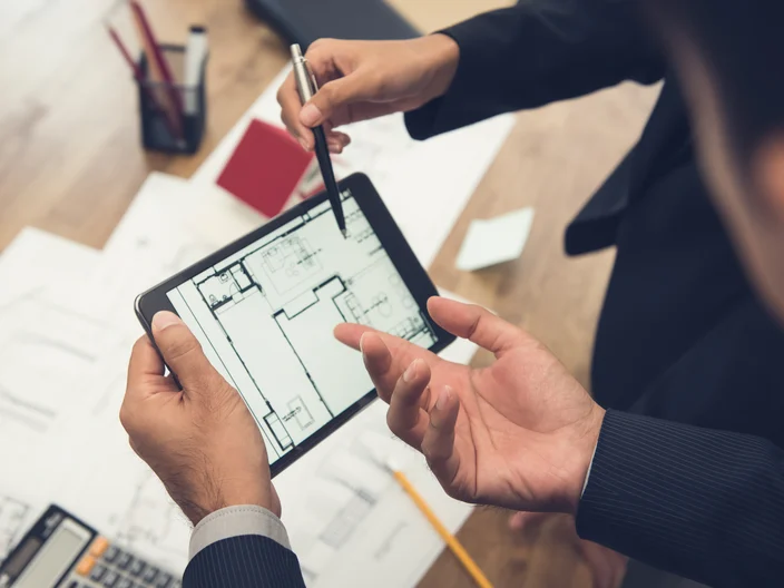 Real estate agent with client or architect team checking a housing model and its blueprints digitally using a tablet