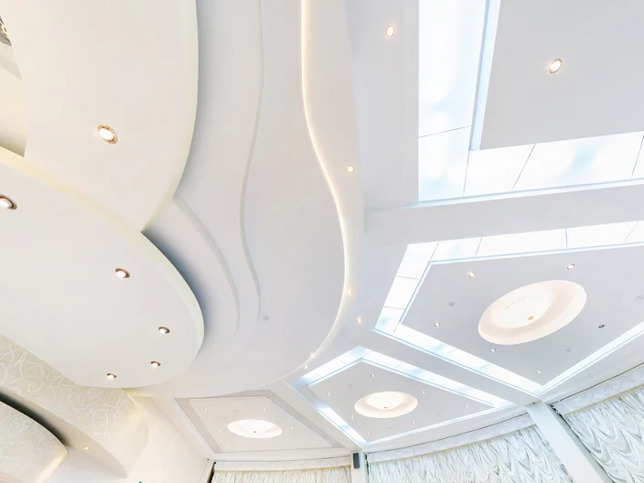 looking up on suspended ceiling with halogen spots lamps and drywall construction in empty room in apartment or house. Stretch ceiling white and complex shape.
