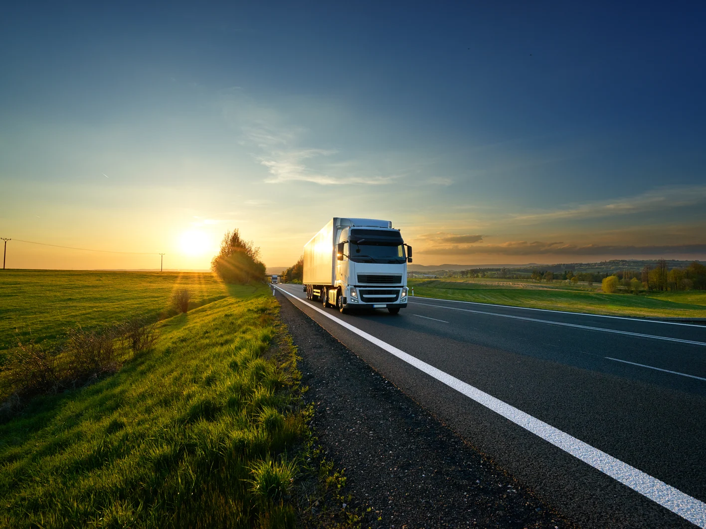 White truck driving on the asphalt road in rural landscape at sunset