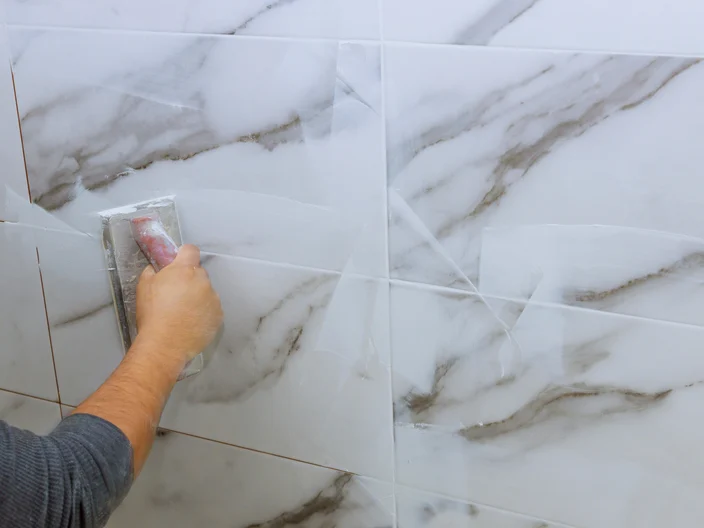 Male hand with the rubber applies grout on a seam between tiles