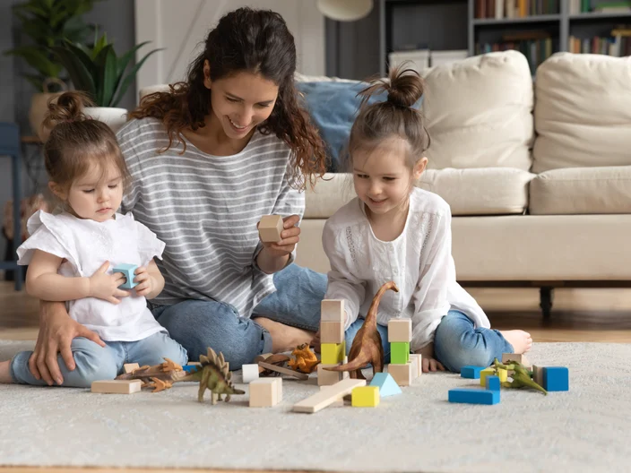 Smiling caring mother playing with two little daughters on floor