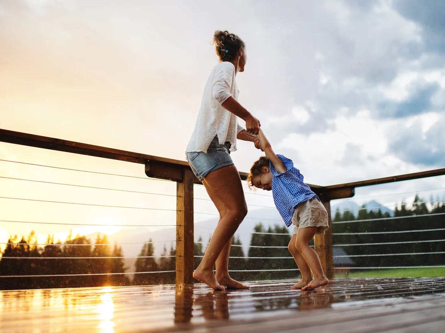 Mother with small daughter playing in rain on patio of wooden ca