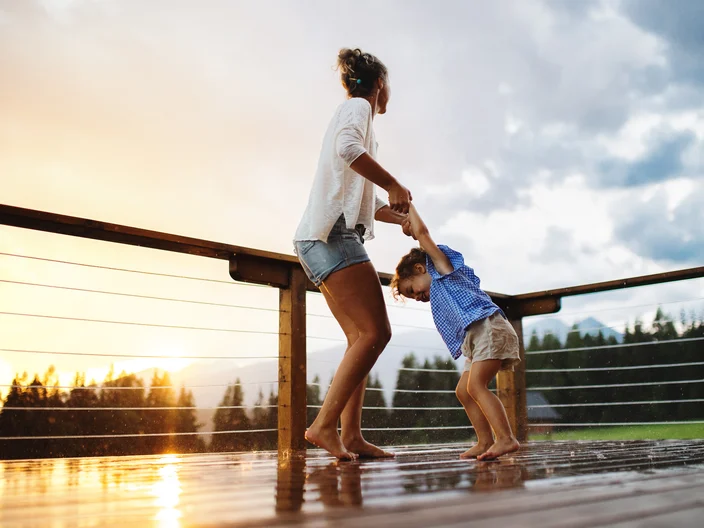 Mother with small daughter playing in rain on patio of wooden ca