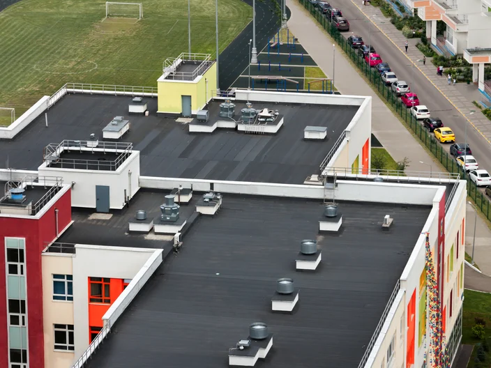 Top view dark flat roof with air conditioners and hydro insulation membranes on top of a modern apartment building residential area.
