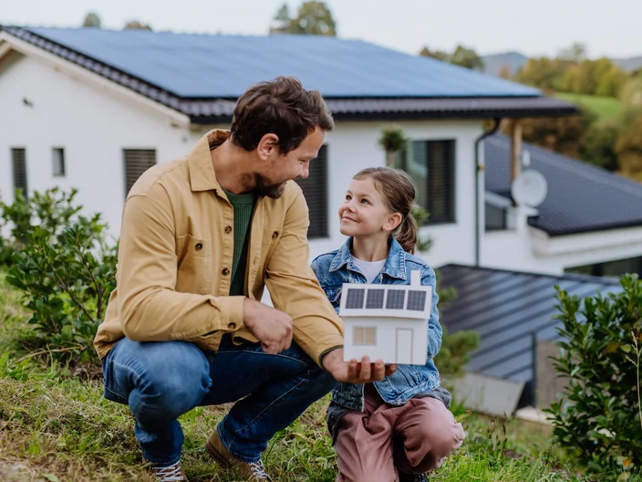 Little girl with her dad holding paper model of house with solar panels, explaining how it works.Alternative energy, saving resources and sustainable lifestyle concept.
